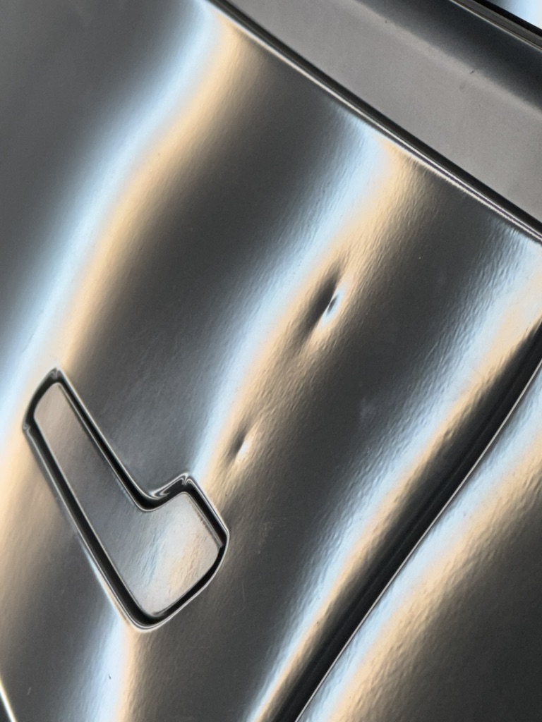 Two small dents beside a black vehicle door handle
