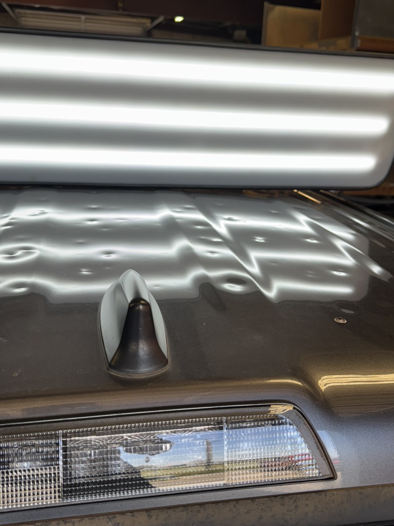 Extensive hail dents across a vehicle roof under an inspection light