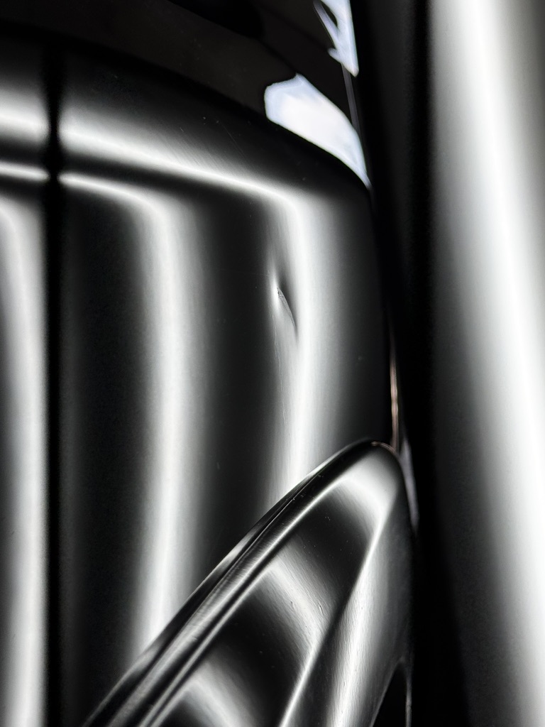 Small sharp dent on a dark vehicle panel under PDR reflection lighting